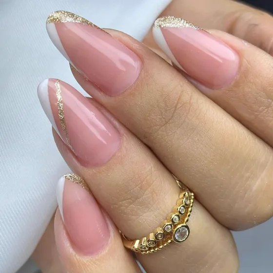 Mão com unhas amendoadas em soft gel, francesinha branca com fio dourado sobre base nude.